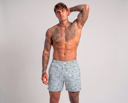 Man wearing light blue swim shorts with a pattern on a plain background