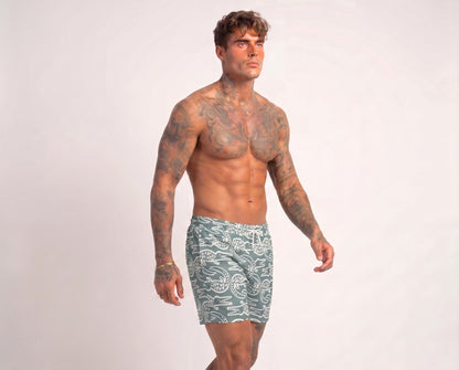 Man wearing green swim shorts with a pattern on a white background