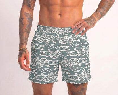 Person wearing green swim shorts with white crocodile pattern on a plain background