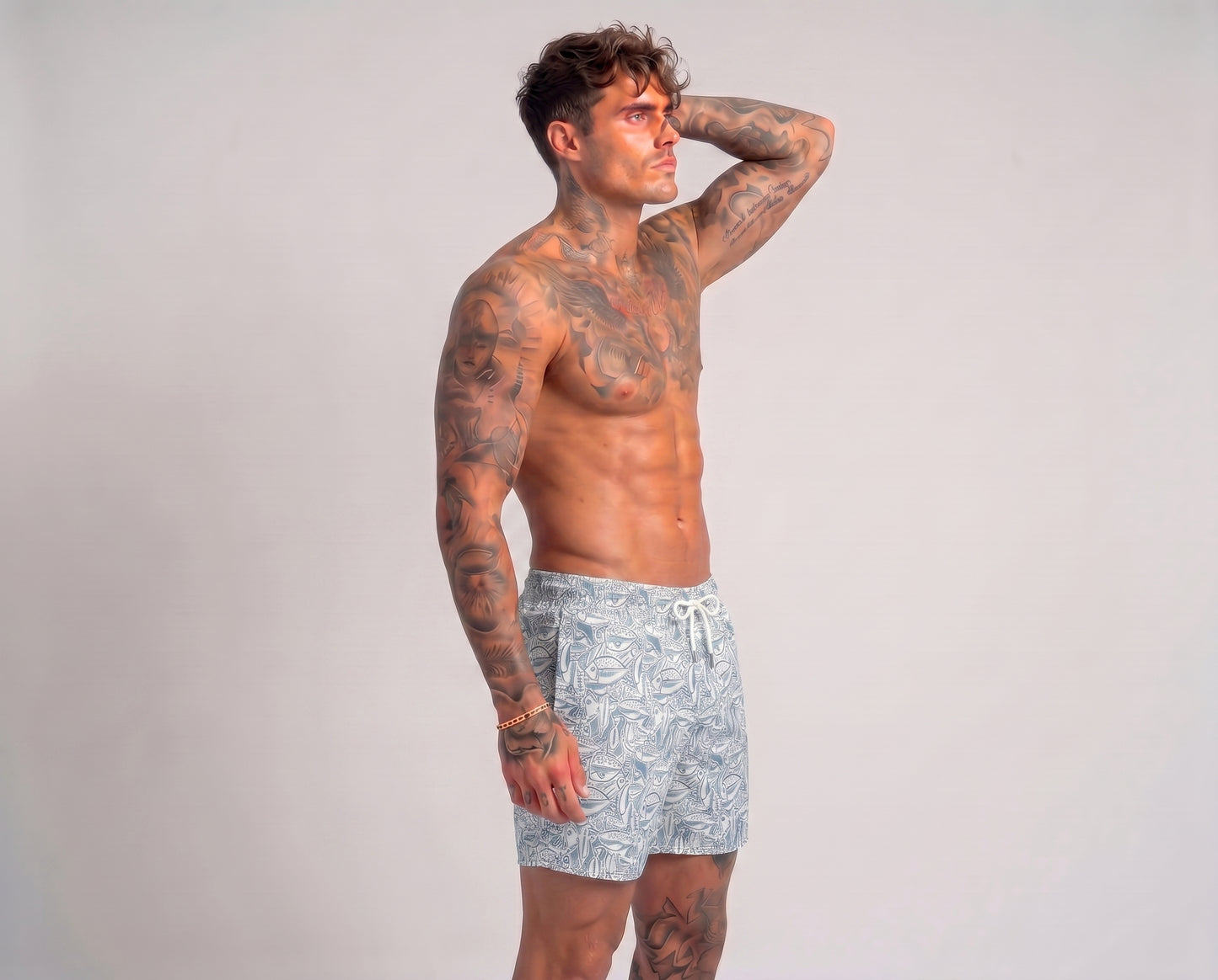Man wearing light blue swim shorts with a pattern on a plain background