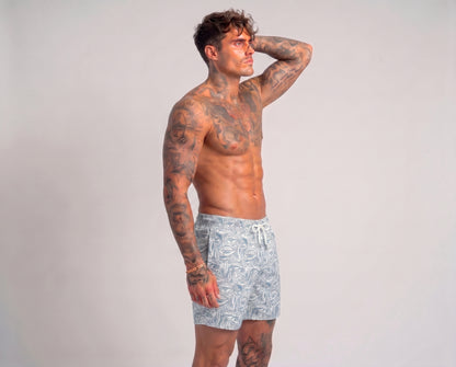 Man wearing light blue swim shorts with a pattern on a plain background