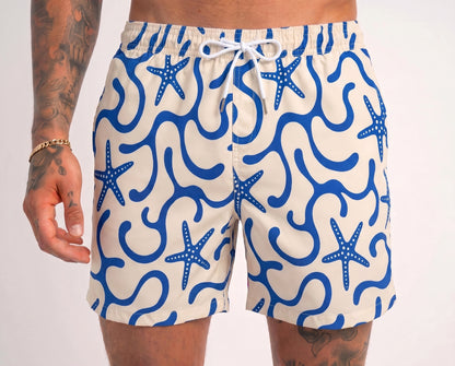Beige swim shorts with blue starfish pattern worn by a person on a white background